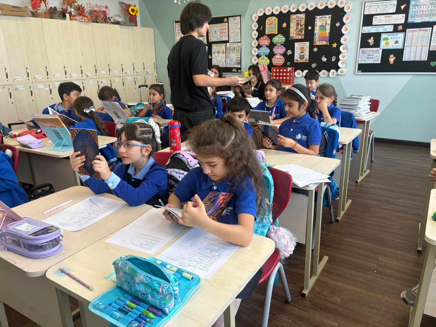Jamal walks between the desks handing out books while pupils look at their copies.