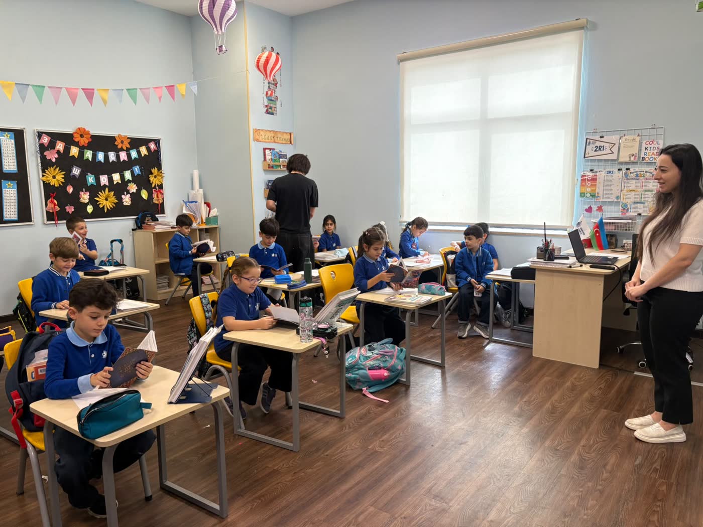Pupils read at their desks while their teacher watches from the front of the room.